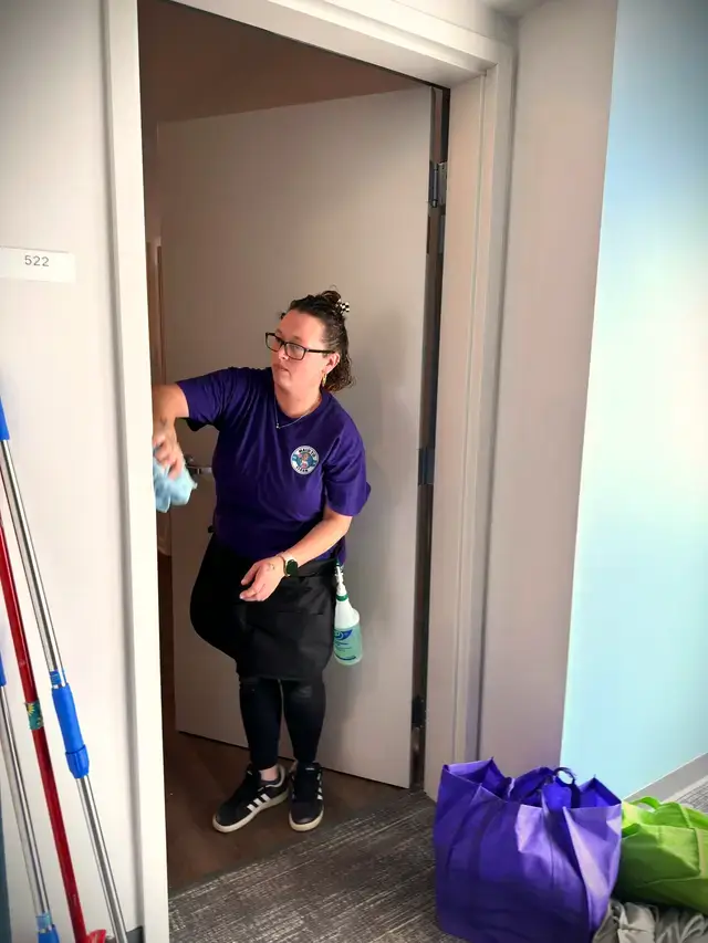 A cleaner with a spray bottle in a doorway, her supplies at her feet
