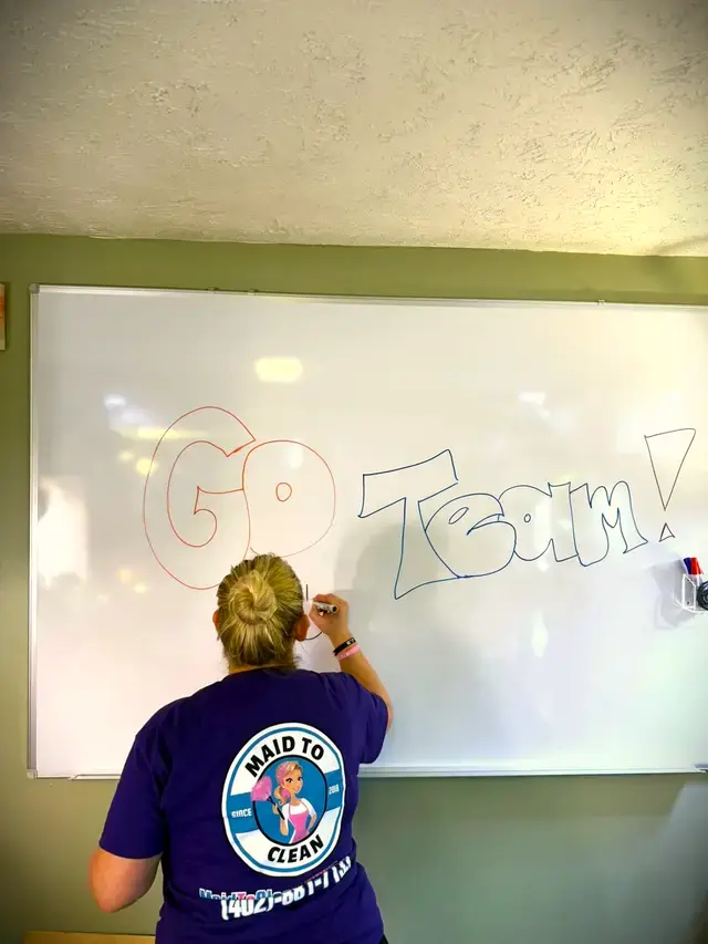 A team member writing GO Team on a whiteboard, the logo on the back of her shirt